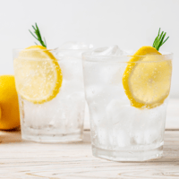 Two glasses filled with a clear beverage and floating lemon slices. 